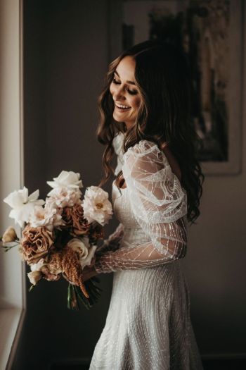 Bride standing by the window holding bunch of flowers at Enzo weddings Hunter Valley