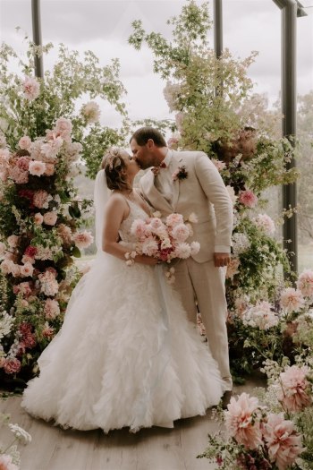 Bride & Groom first kiss at Chapel Ridge wedding venue surrounded by magnificent florals