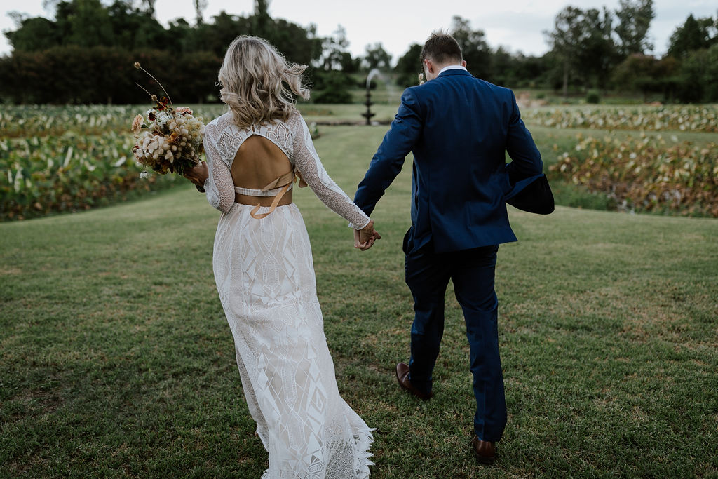 Just married couple holding hands walk through the beautiful gardens of Albion Farm