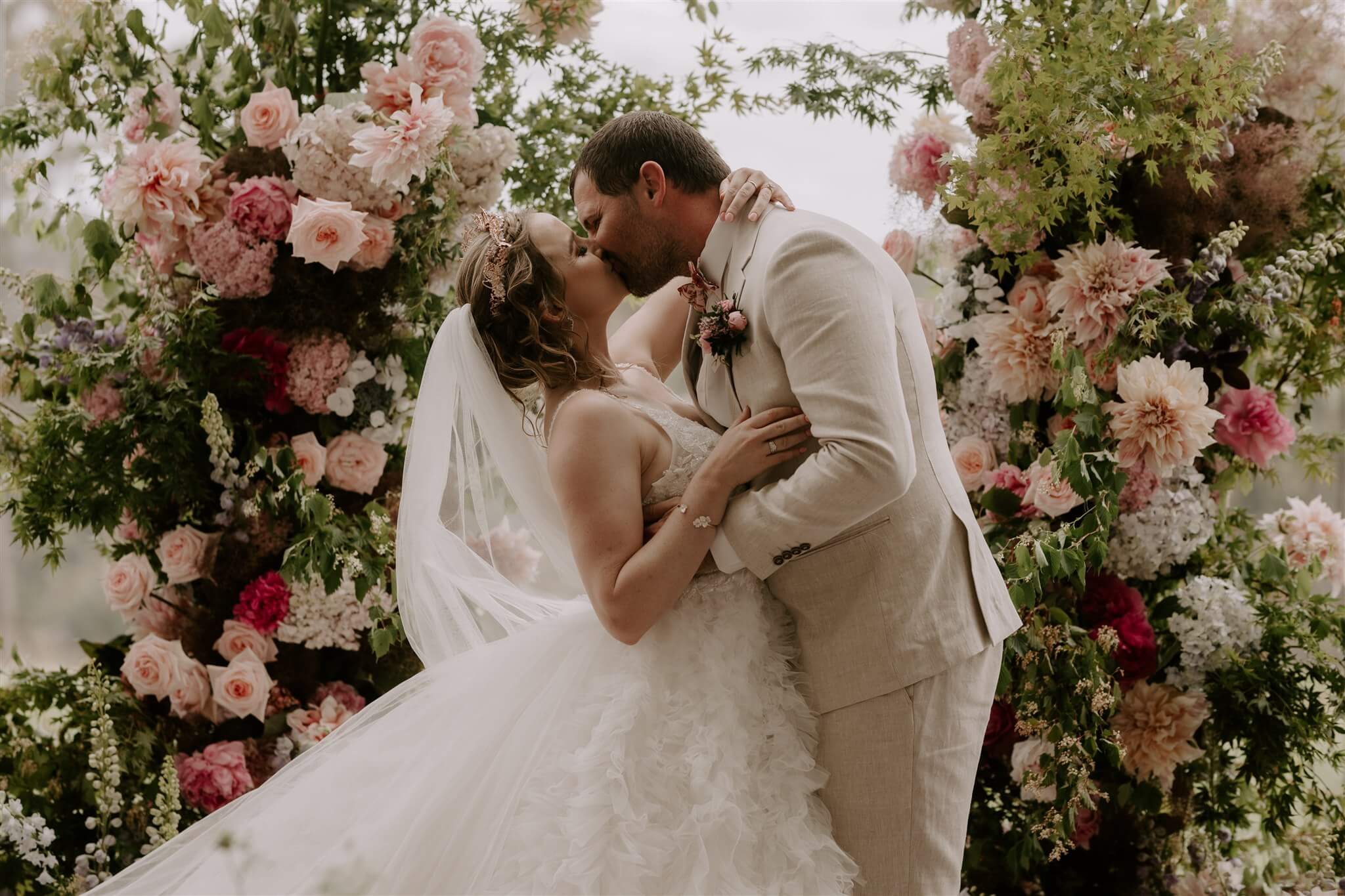 Bride and Groom kiss after their ceremony in front of magnificent backdrop of coloured flowers at Chapel Ridge wedding venue