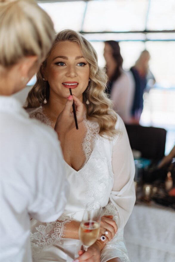 Wedding makeup artist applying brides red lipstick to the brides lips on her wedding day at Chapel Ridge
