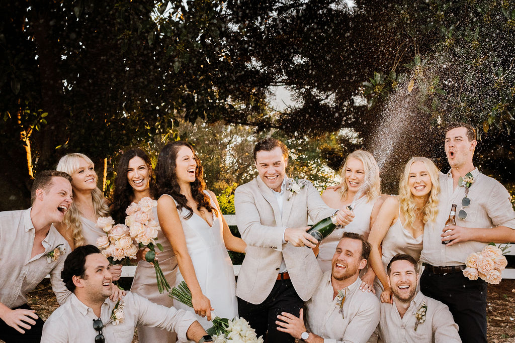 Bridal party laughing and popping champagne at Hunter Valley wedding venue Wallalong House
