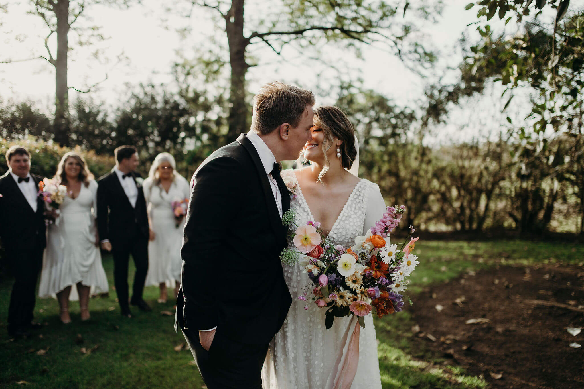 Bride and Grooms stroll through gardens at sunset with bridal party in tow